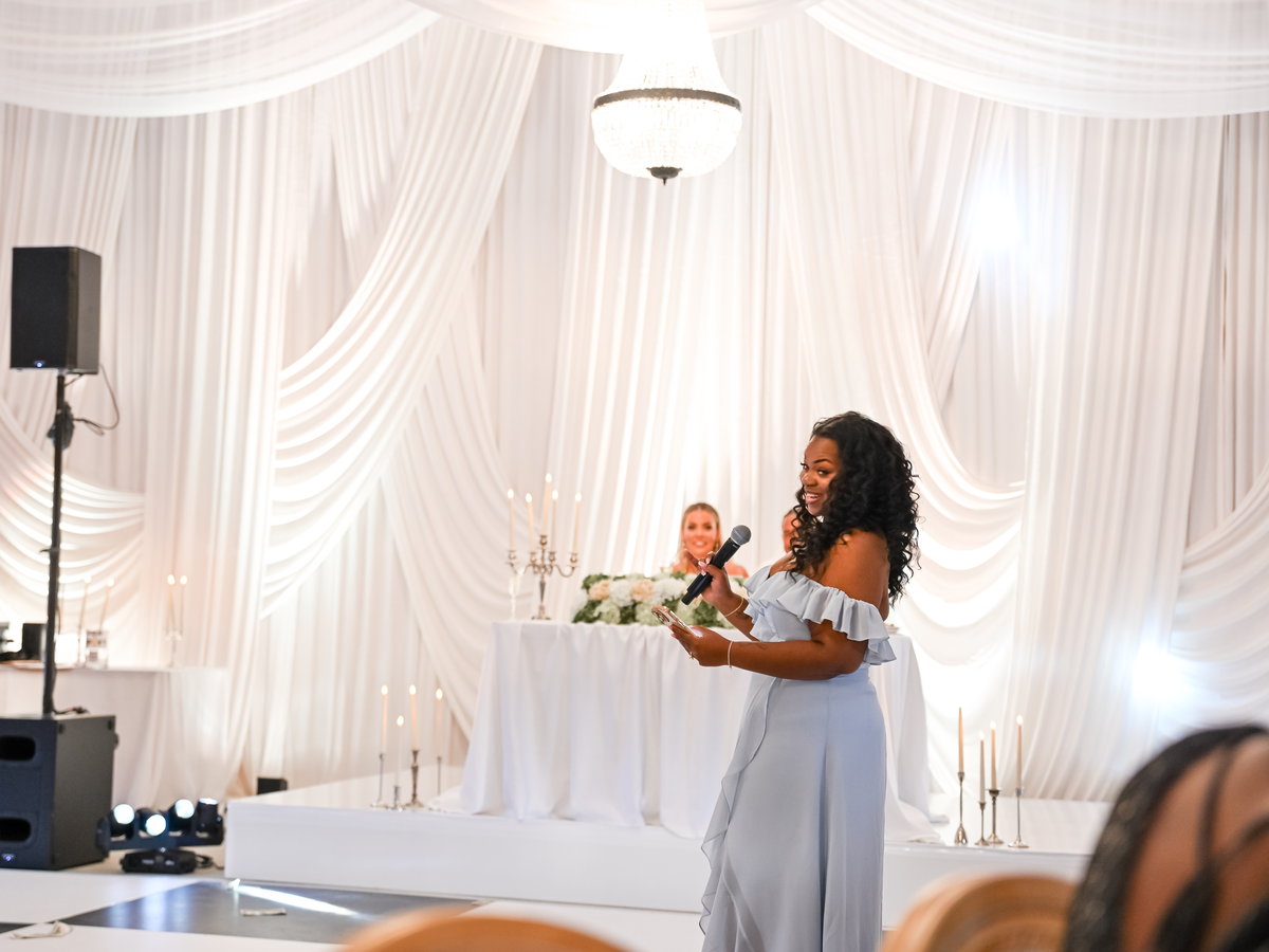 A guest giving a toast in front of the white draped backdrop